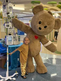 Child in the hospital hugging a giant teddy bear mascot